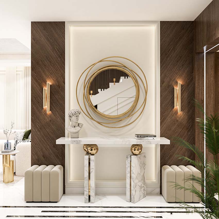 Opulent entryway featuring a modern circular gold mirror framed by artistic golden spirals on a cream backdrop, flanked by dark wooden accents and elegant sconces, illustrating contemporary interior design.